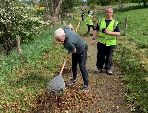 A group of volunteers wearing hi-vis tabards, tidy up a local footpath.